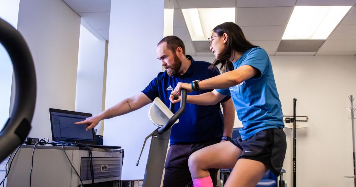 Participant performing exercise test while faculty member monitors and points to results on computer screen